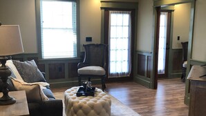 A living room with a sofa, ottoman, and chair, wooden flooring, and a ceiling fan. - Guest quarters at the inn - 205 (North Beach)