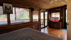 A cozy cabin room with a large bed, wooden walls, a ceiling fan, and a television on a wooden cabinet. - 4WD / AWD Adventure For 2 - Private Setting Near Great Smoky Mtns National Park (Sevierville)