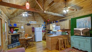 A rustic cabin interior with a wooden ceiling, a fireplace, a dining area, kitchen, and a green wall with a painting. - 4WD / AWD Adventure For 2 - Private Setting Near Great Smoky Mtns National Park (Sevierville)