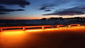 En strandpromenade i skumringen med gelænder og siddepladser.
