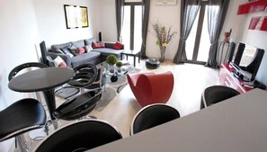 Una sala de estar moderna con un sofá gris, sillas negras y rojas, una mesa de centro y un televisor.