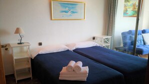 Ein Hotelzimmer mit zwei Betten, einem Nachttisch mit Lampe, einem kleinen Tisch und einem Stuhl.