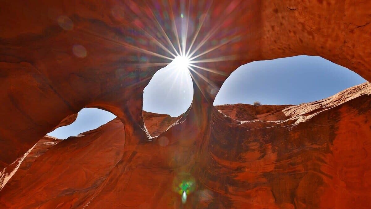 A natural rock formation with a clear sky and sunlight shining through.