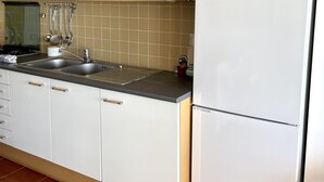 A kitchen with white cabinets, a stainless steel sink, and a white refrigerator with a logo.