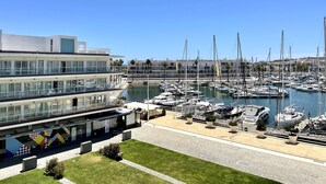 A marina with multiple boats docked, a modern building with large windows, and a clear blue sky.