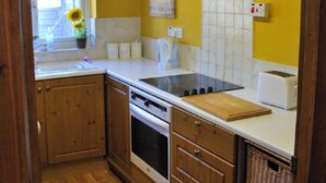 A kitchen with wooden cabinets, a stove, a sink, and a window with sunflowers.