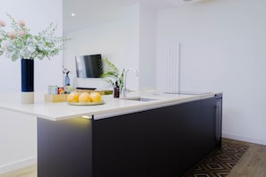 A modern kitchen with a white countertop, black cabinets, a built-in sink, and a potted plant. - Luxurious apartment of 130 sqm completely refurbished and equipped for mid to long term stays. (Madrid)