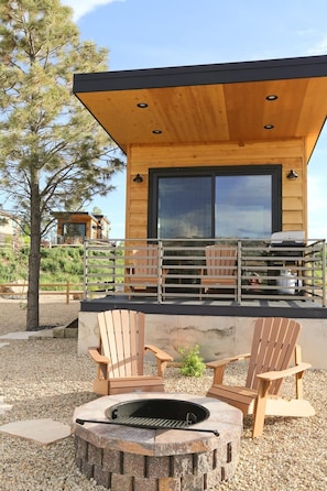 Une cabane moderne en bois, dotée d’une grande fenêtre, d’un espace salon extérieur et d’un foyer.
