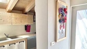 A modern kitchen with wooden beams, a skylight, a sink, and a colorful artwork on the wall.