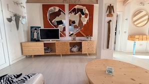A modern living room with a wooden TV stand, a heart-shaped wall art, and a round wooden table.