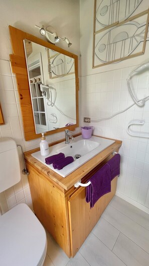 Ein Badezimmer mit einem Holzkosmetikschrank, einem weißen Waschbecken, einem Spiegel, einer Toilette und einem Handtuchhalter.