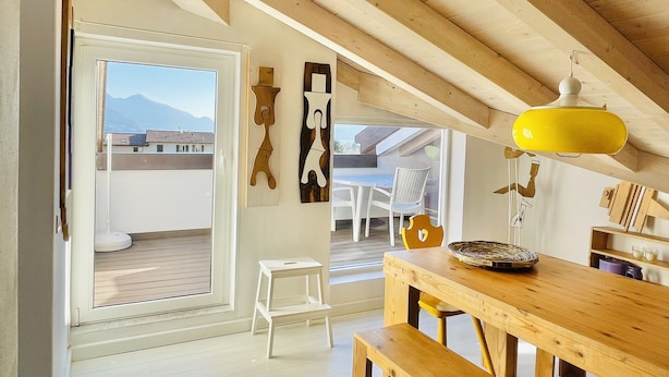 A spacious room with a wooden ceiling, a dining table with benches, a white chair, and a small white stool.