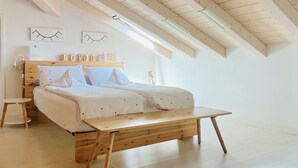 A bedroom with a wooden ceiling, a bed with white bedding, and a small table.