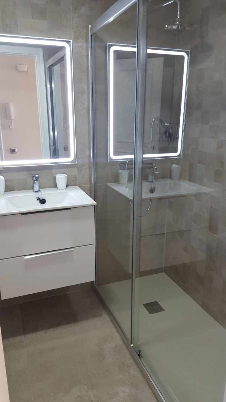 Un baño moderno con cabina de ducha de vidrio, tocador blanco con espejo y salpicadero de azulejos.