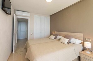 A bedroom with two beds, a bedside table with a lamp, and a TV mounted on the wall.