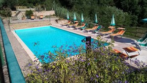 A swimming pool with lounge chairs and umbrellas, surrounded by greenery and a stone wall. - Period residence in medieval town in the center of Tuscany (Palaia)