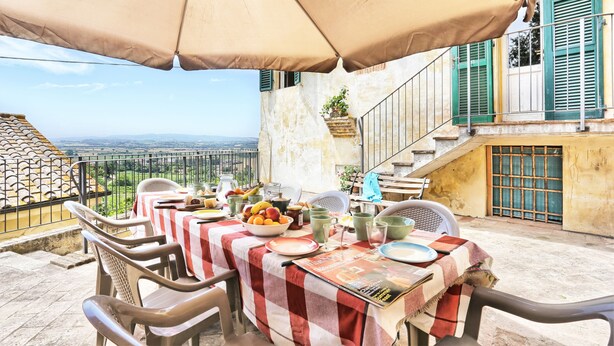 An outdoor dining area with a table set for two, covered by a large umbrella, overlooking a scenic view. - Period residence in medieval town in the center of Tuscany (Palaia)