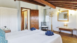 A bedroom with a large bed, wooden ceiling beams, a wooden chair, a small table with a lamp, and a mirror on the wall. - Period residence in medieval town in the center of Tuscany (Palaia)