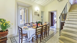 A dining area with a round table set for four, surrounded by wooden chairs. A potted plant with yellow flowers is on the left. - Period residence in medieval town in the center of Tuscany (Palaia)