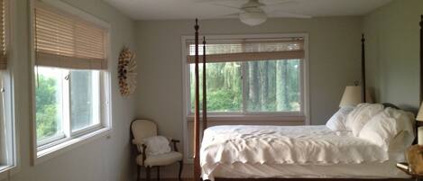 A bedroom with a four-poster bed, a chair, a standing lamp, and a ceiling fan.