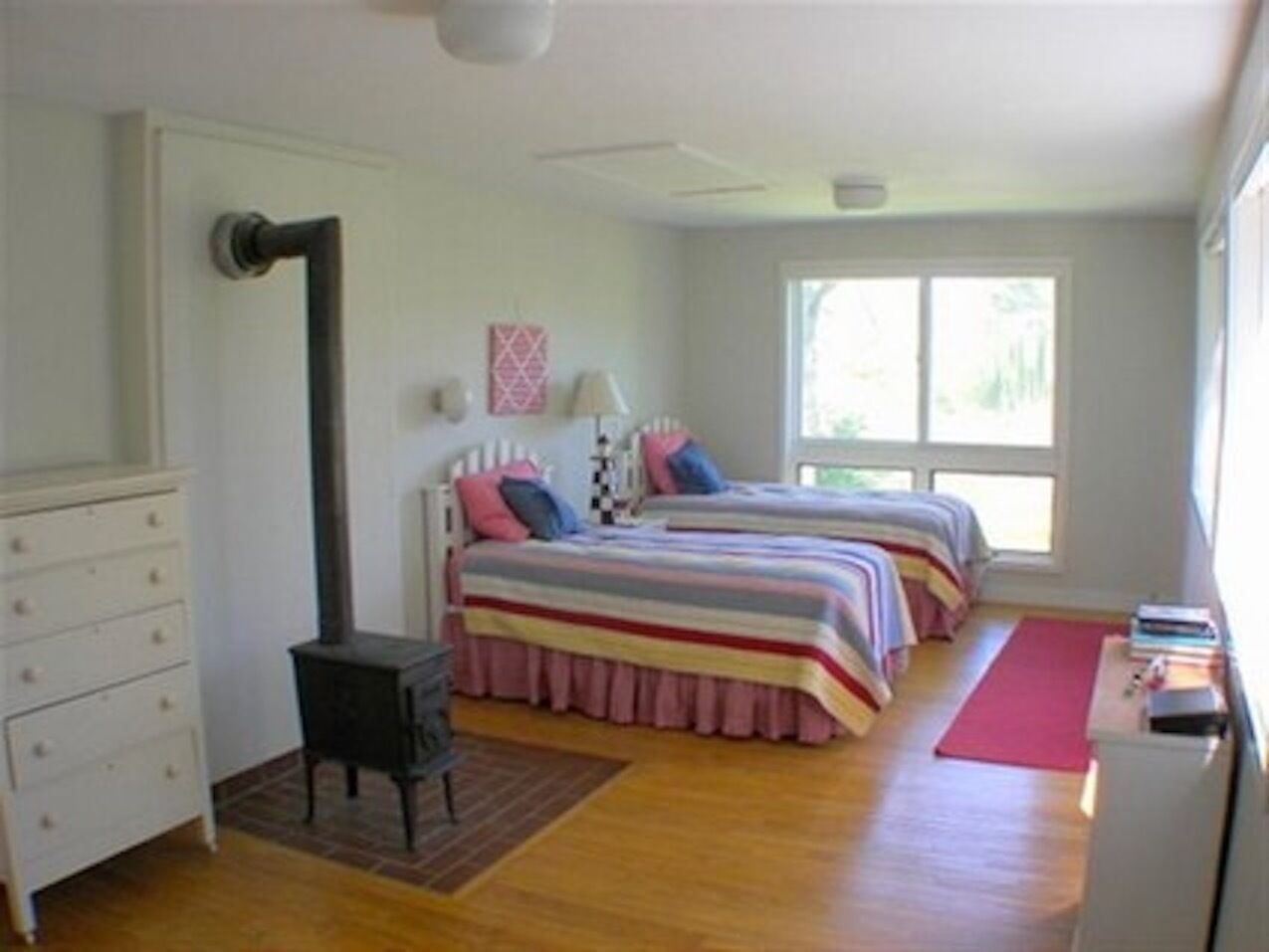 A bedroom with two beds, a dresser, a small table, and a window.