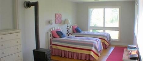A bedroom with two beds, a dresser, a small table, and a window.