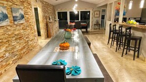 A long dining table with chairs, a kitchen area, and a stone wall with artwork. - ASK ABOUT Sept-Oct2026 SPECIAL! 14Bd10Bth Home Comfortably Accommodates Up to 30 (Marathon)