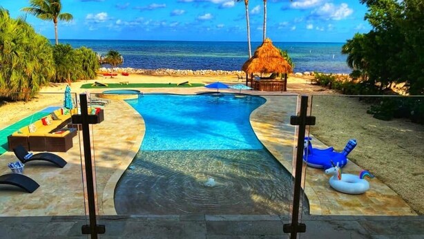 A swimming pool with a view of the ocean, surrounded by lounge chairs and palm trees. - ASK ABOUT Sept-Oct2026 SPECIAL! 14Bd10Bth Home Comfortably Accommodates Up to 30 (Marathon)