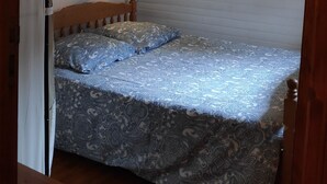 Ein Einzelbett mit gemustertem Überwurf, eine Nachttischlampe und ein gerahmtes Bild an der Wand.