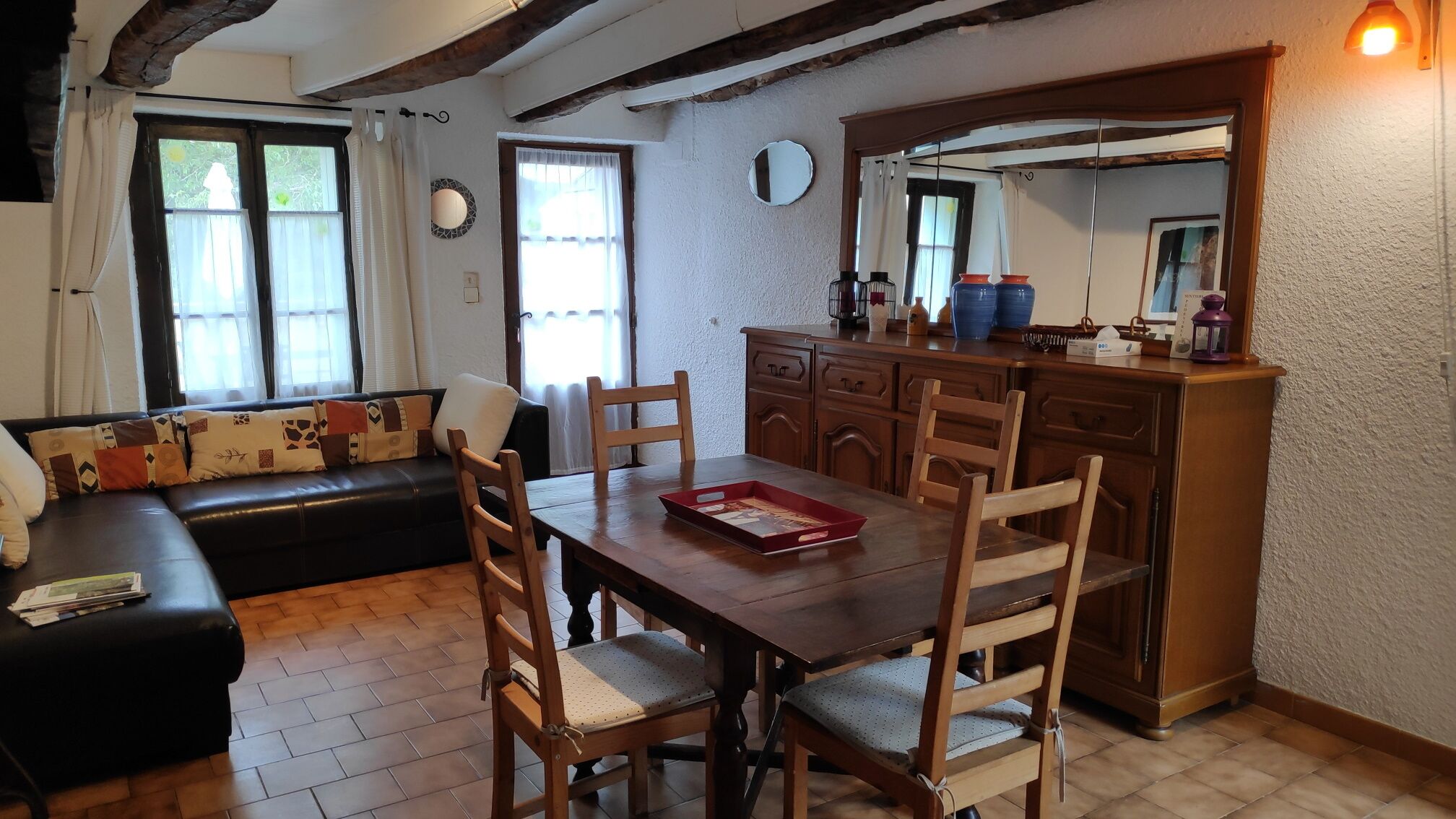 Una sala de estar acogedora con una mesa de comedor de madera, sillas, un sofá y una cocina con armarios y un espejo.