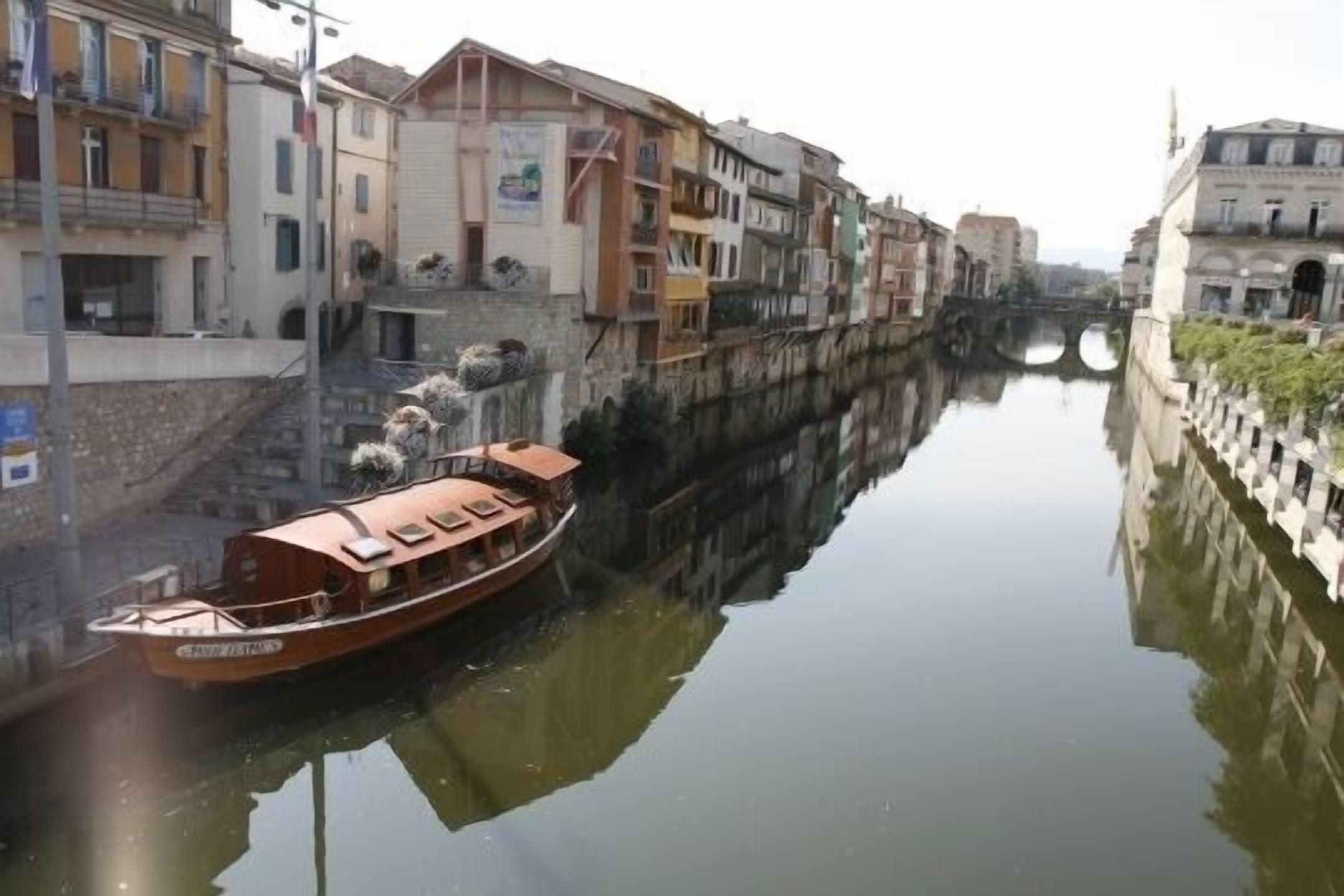 A narrow canal with a boat docked on the left, surrounded by multi-story buildings with balconies and windows.