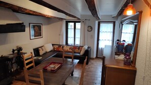 Ein gemütliches Wohnzimmer mit einem Holztisch, zwei Sofas, einer Nähmaschine und einem Fenster mit Vorhängen.