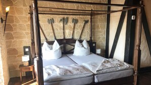 A four-poster bed with a stone wall backdrop, a bedside table with a lamp, and a small nightstand. - Interesting holiday apartment GUARDROOM in the Leppersdorf manor (Wachau)