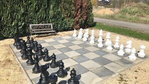 A large outdoor chessboard set up on a paved area with a bench and greenery in the background. - Interesting holiday apartment GUARDROOM in the Leppersdorf manor (Wachau)