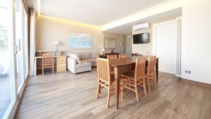 A modern living room with a dining area, a sofa, a desk, and a TV mounted on the wall. - SUITE WITH VESUVIUS VIEW TERRACE IN HISTORIC CENTER (Napoli)