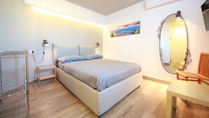 A bedroom with a bed, bedside lamps, a small table, a mirror, and a painting on the wall. - SUITE WITH VESUVIUS VIEW TERRACE IN HISTORIC CENTER (Napoli)