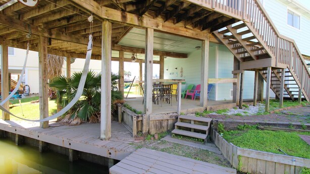 Una terraza de madera con una escalera que lleva a un espacio cubierto con sillas y mesas.