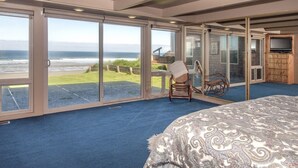Un dormitorio con una cama grande, una silla y un televisor. Tiene vista al océano a través de amplios ventanales.