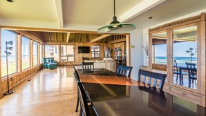Un comedor amplio con una larga mesa de madera, sillas y ventanas grandes que ofrecen vistas al océano.