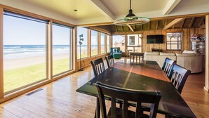 Un comedor espacioso con una mesa larga y sillas, ventanas grandes con vistas a la playa y decoración de madera.