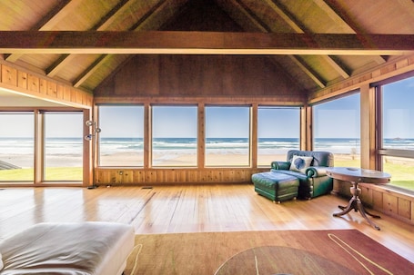 A room with a wooden ceiling, large windows, a green leather sofa, and a small table.. Oceanfront beach house with direct beach access In the desired Roads End area