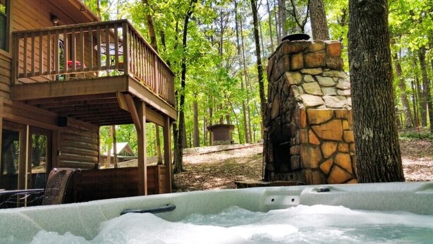 A cabin with a hot tub, a stone fireplace, and a deck overlooking a forest. - At Last, you can enjoy life with all the comforts of your own home on your stres (Broken Bow)