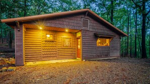 A wooden cabin with a large garage door, a small attached shed, and a gravel driveway. - At Last, you can enjoy life with all the comforts of your own home on your stres (Broken Bow)