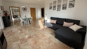 A modern living room with a black sofa, a dining table with chairs, and a kitchen in the background. - The terrace - vacation home with lake view (San Zeno di Montagna, Verona)