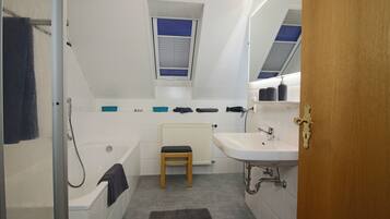 A modern bathroom with a bathtub, a small wooden stool, a window, and a radiator.
