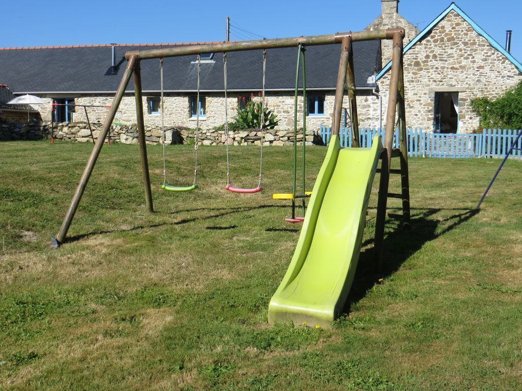 A swing set with a green slide in a grassy yard with a stone building in the background.