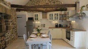 A kitchen with stone walls, wooden beams, white cabinets, and a dining table set for four.