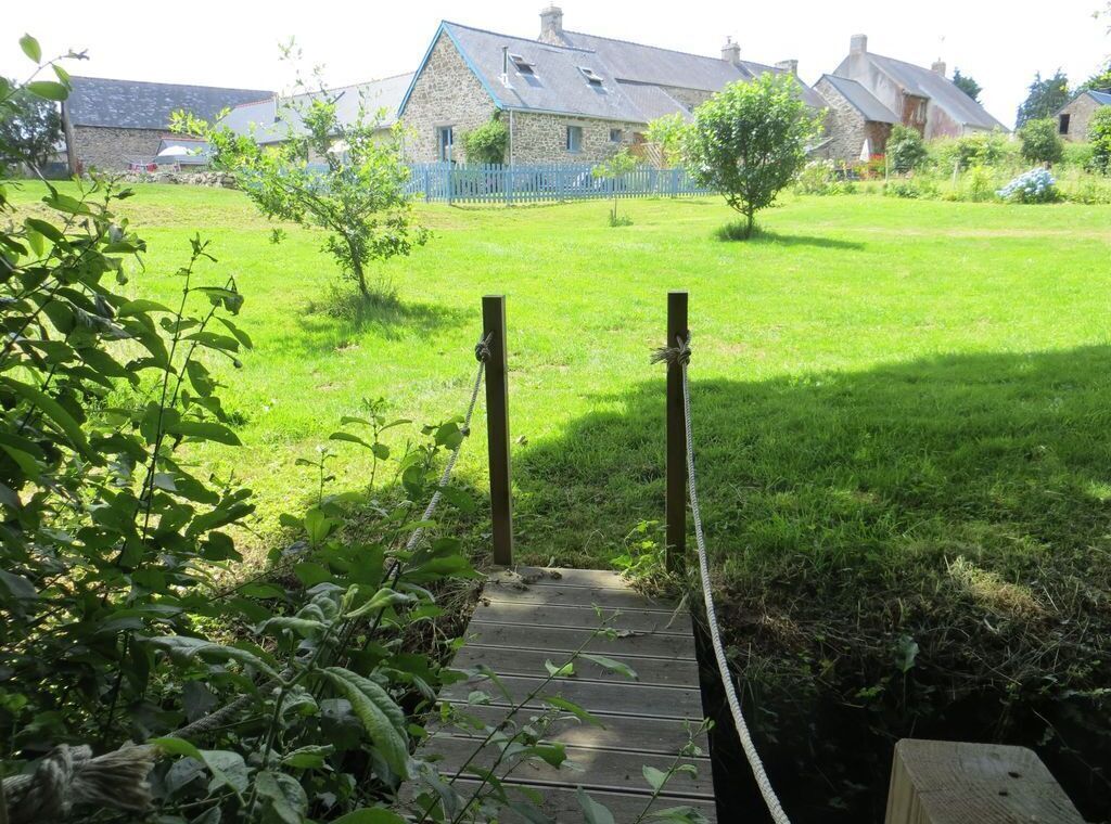 A wooden bridge leading to a grassy area with stone buildings in the background.