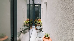 Een smalle gang met een glazen deur die uitkomt op een balkon, met potplanten en metalen stoelen.