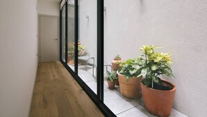 Een smalle gang met houten vloeren, grote glazen deuren die leiden naar een balkon met potplanten en een kleine tafel.